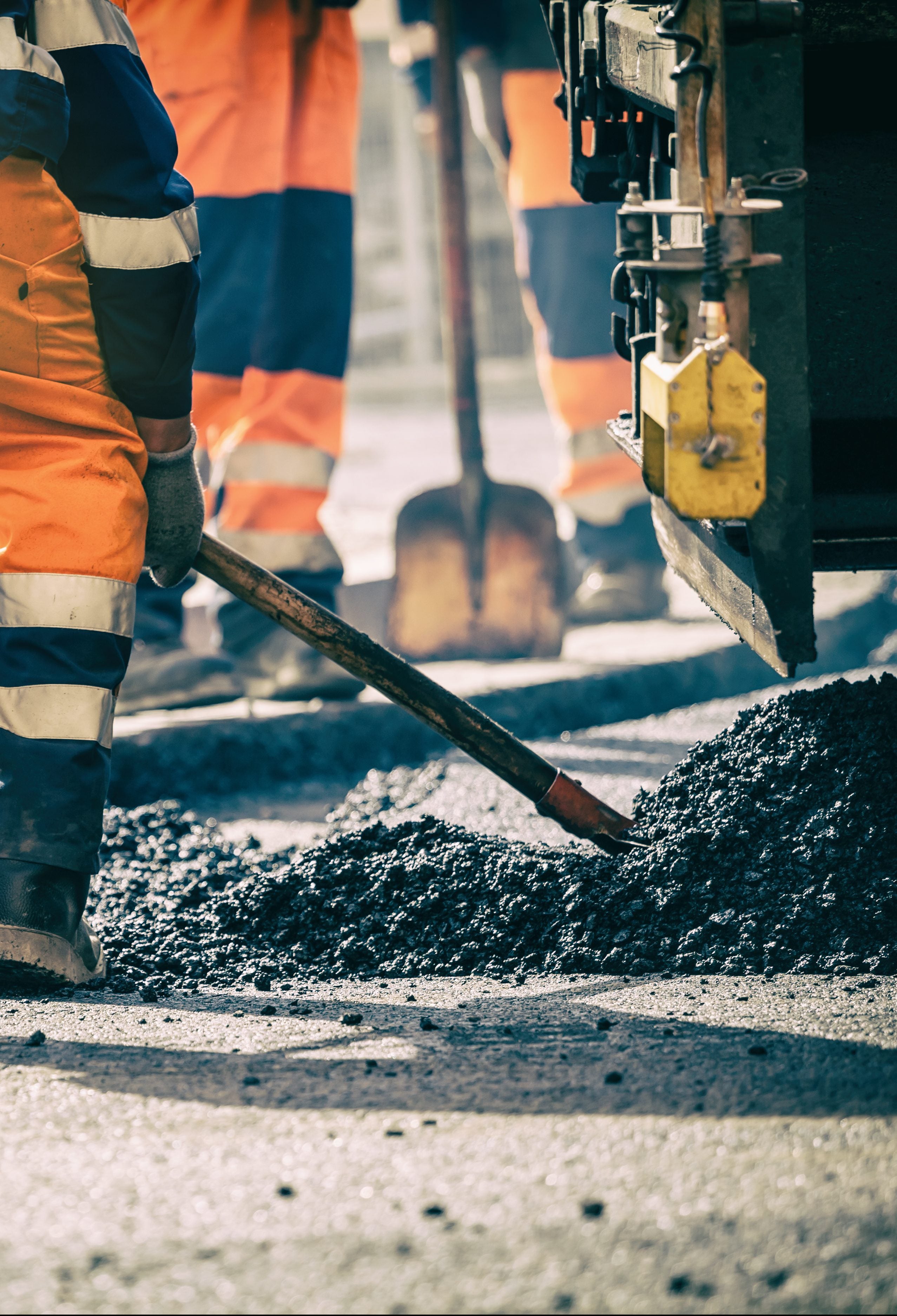 A worker lifts asphalt with his shovel. 